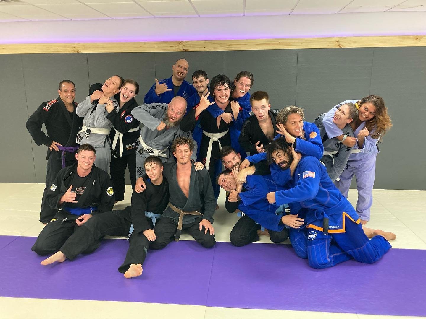 Fifteen adult students in gis smiling together on the purple and white mats at Mentality Martial Arts.