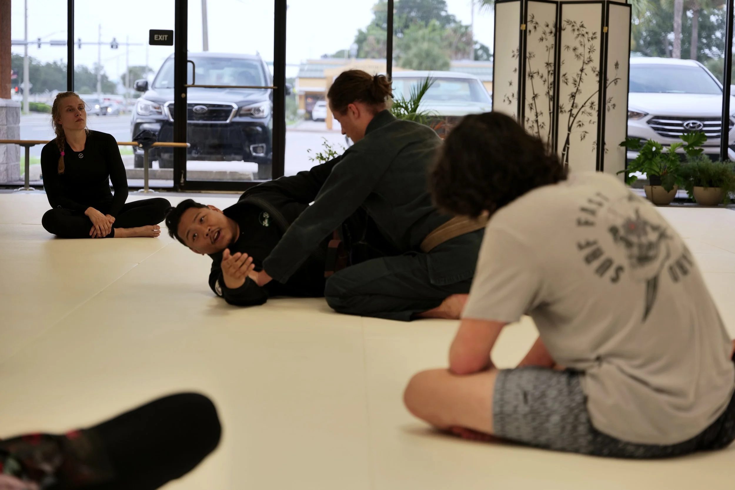 Instructor demonstrating guard technique to adult students during daytime gi class.