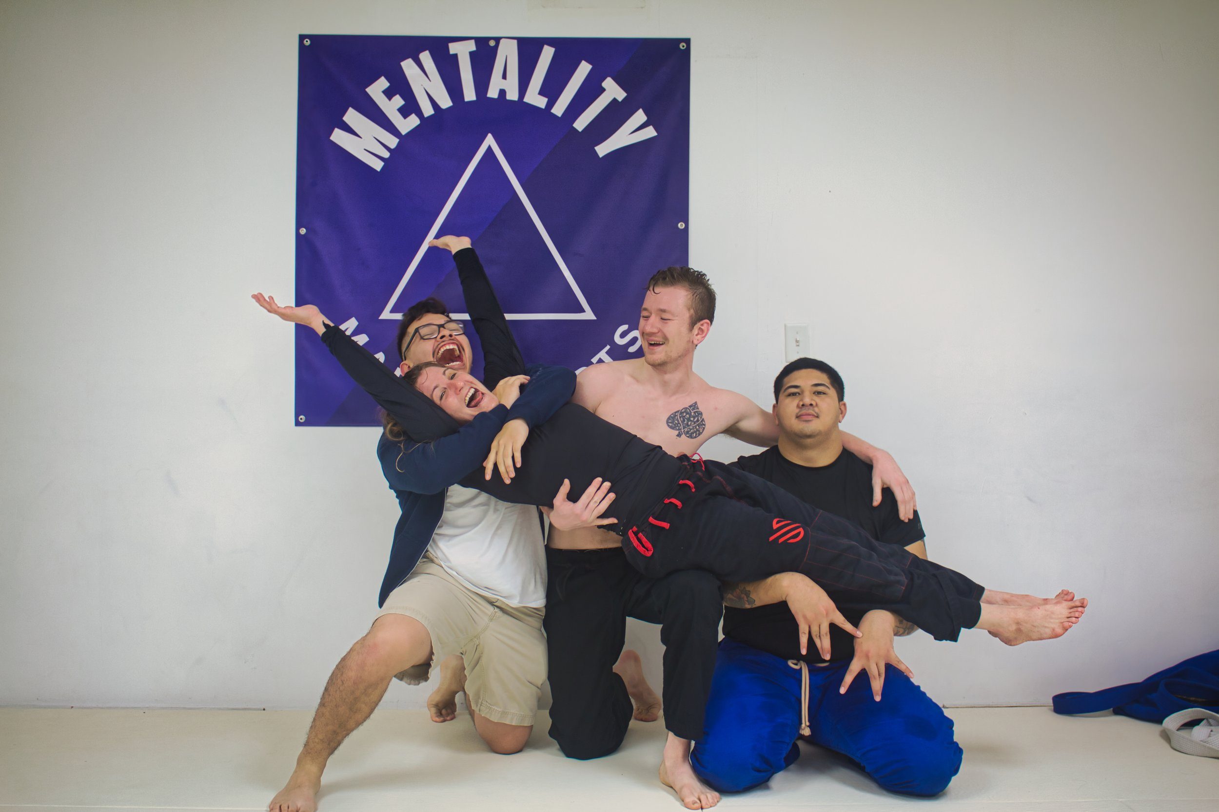 Four adult students laughing in front of the purple Mentality Martial Arts wall banner.