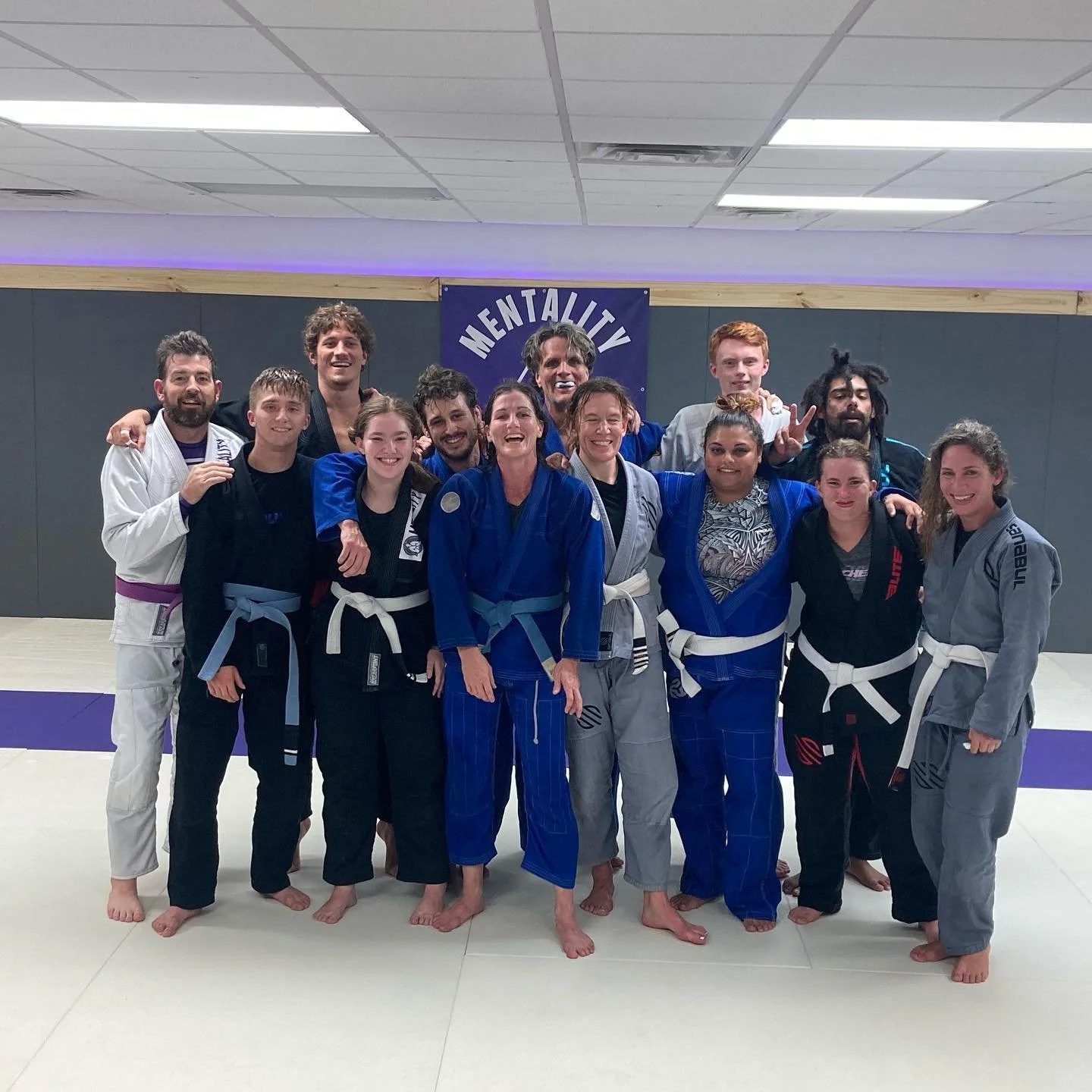 Eleven adult students in white, blue, grey, and black gis standing together after class.